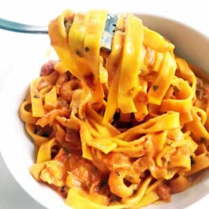 Creamy saffron arrabiata shrimp with tagliatelle with a fork in a white bowl on a white table surface