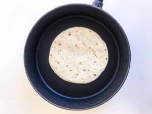 Step one of cooking Chicken Quesadillas - Tortilla in a black pan on a white surface