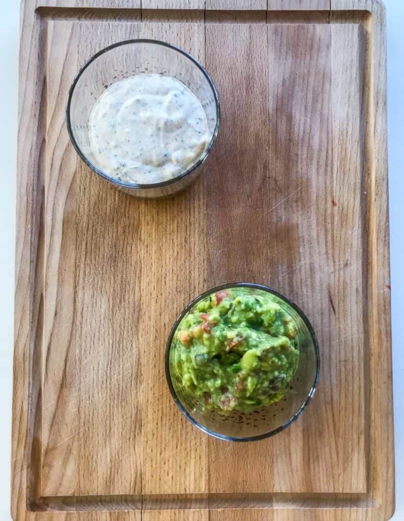 Ranch dip and guacamole for Chicken Quesadillas on a wooden chopping board on a white surface