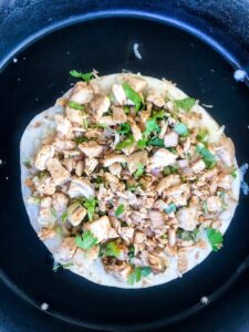 Step three of cooking Chicken Quesadillas - Tortilla topped with cheese and chicken in a black pan on a white surface