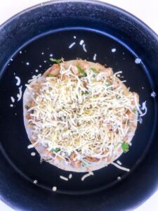 Step four of cooking Chicken Quesadillas - Tortilla topped with chicken and cheese in a black pan on a white surface