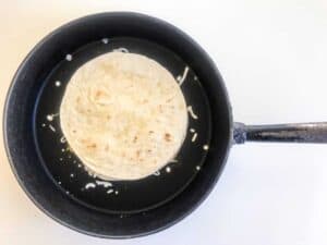 Step five of cooking Chicken Quesadillas - Uncooked quesadilla in a black pan on a white surface
