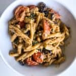 Red pesto pasta with roasted veggies in a bowl on white surface