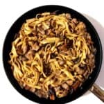 Creamy red wine chicken pasta with chanterelles and white button mushrooms in black pan on white surface