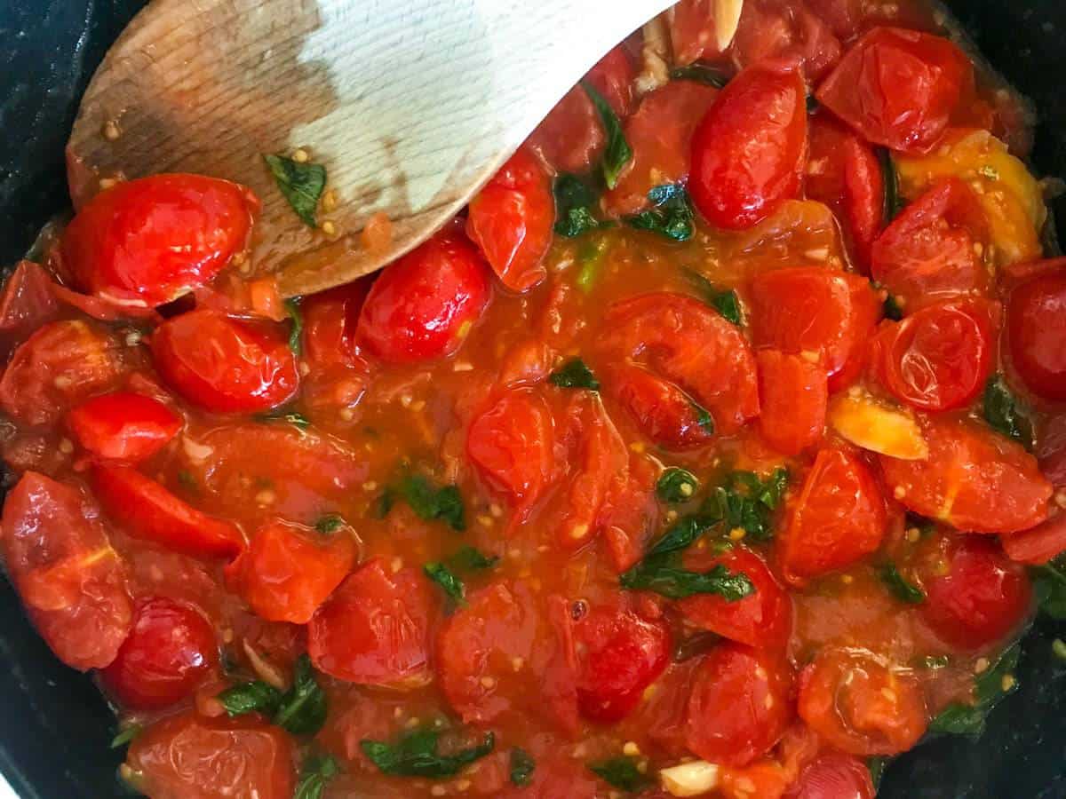 15-minute cherry tomato pasta with spinach and walnuts in a black skillet with a wooden spoon