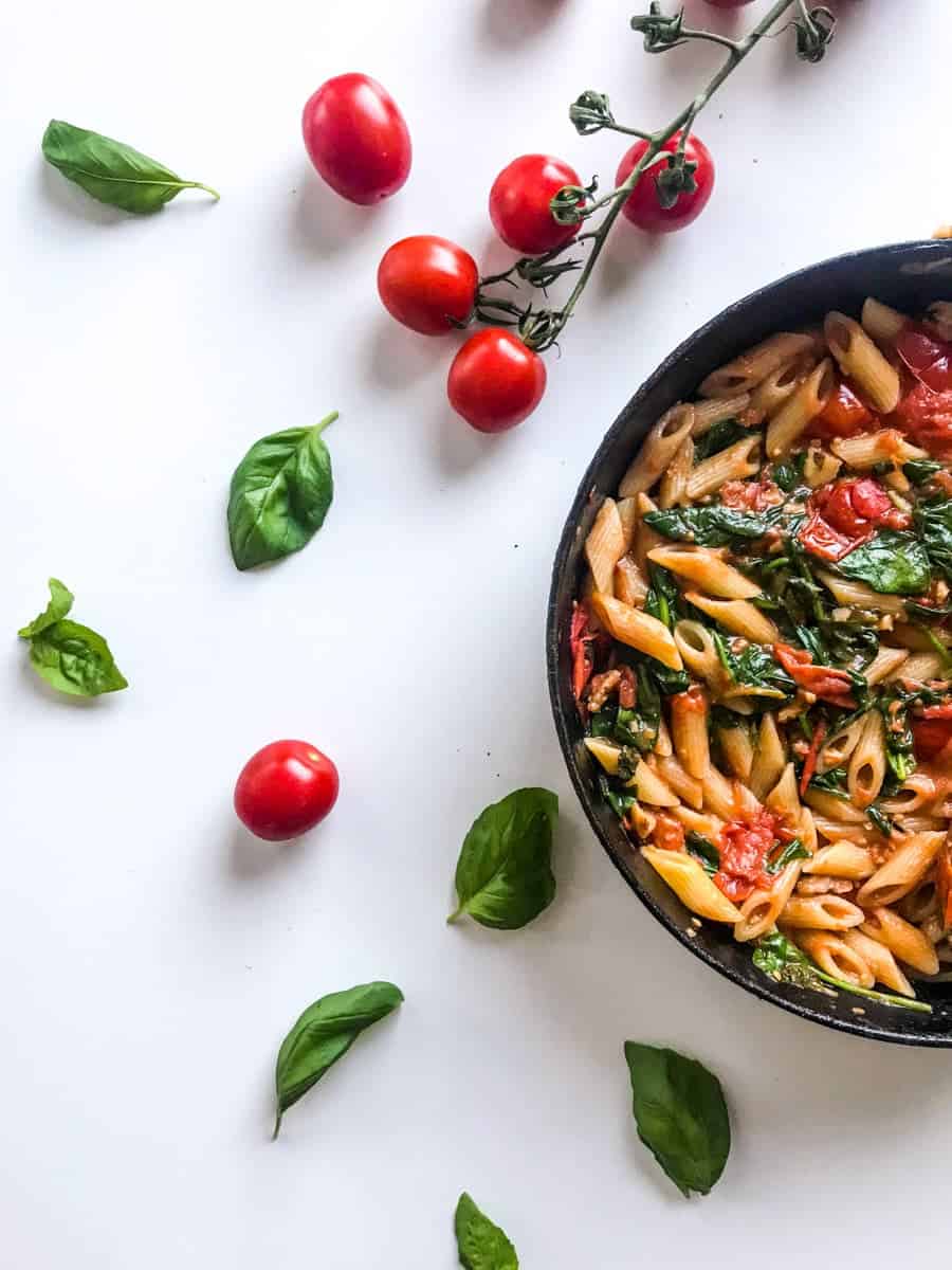 15-minute cherry tomato pasta with spinach and walnuts in a black skillet on a white table decorated with cherry tomatoes on a branch and basil leaves