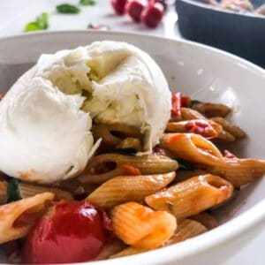 15-minute cherry tomato pasta with spinach and walnuts in a white bowl on a white table decorated with cherry tomatoes on a branch and basil leaves and a black skillet