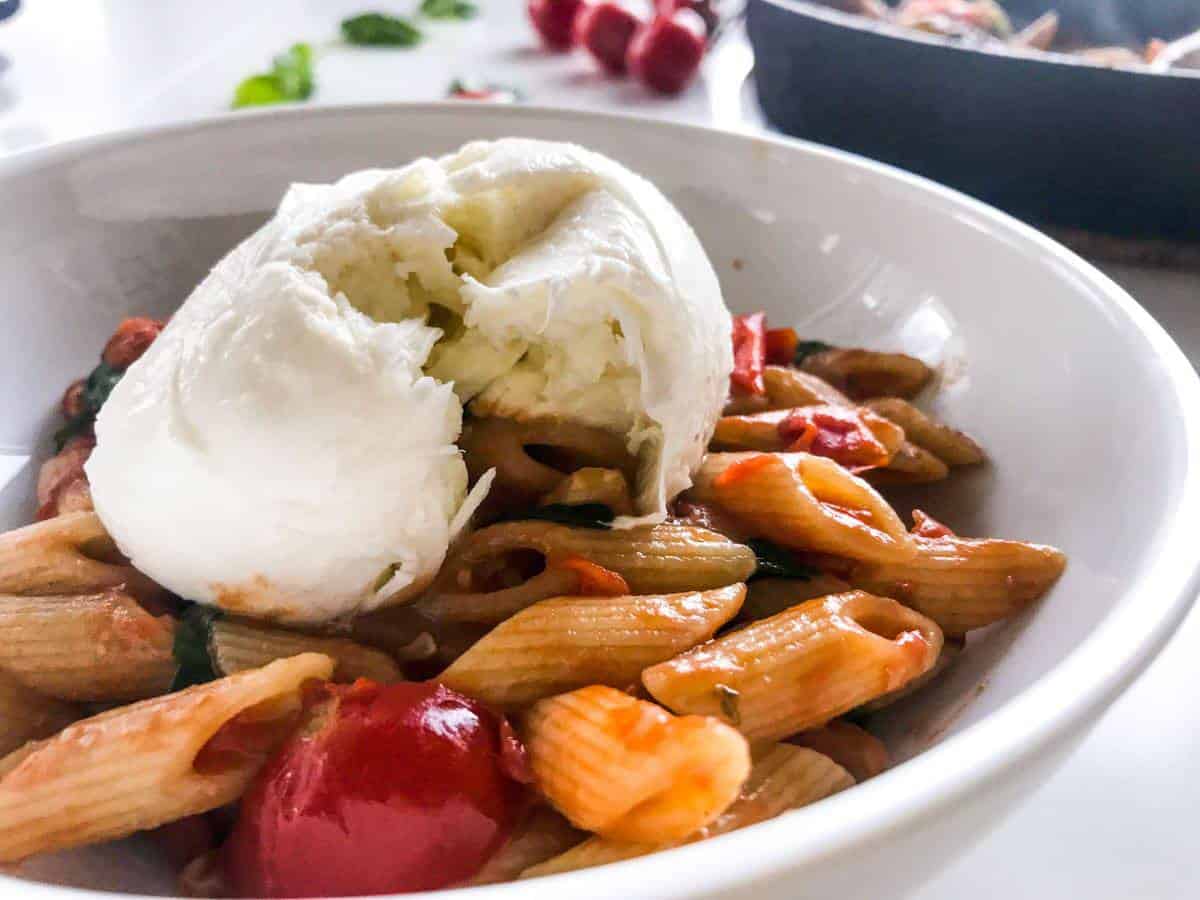 15-minute cherry tomato pasta with spinach and walnuts in a white bowl on a white table decorated with cherry tomatoes on a branch and basil leaves and a black skillet