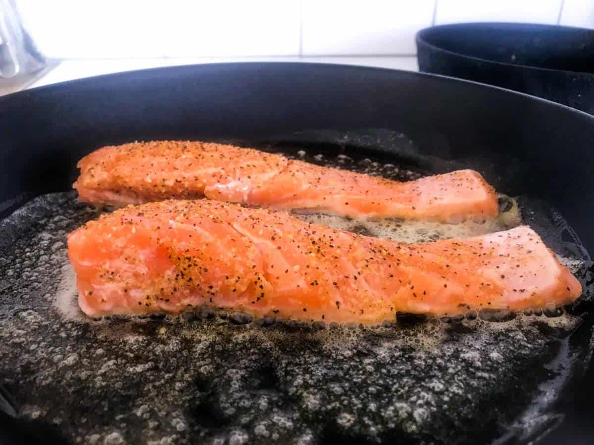 Raw lemon pepper salmon in a cast iron pan for Lemon Pepper Salmon with Garlic Roasted Broccoli and Feta Yoghurt Sauce