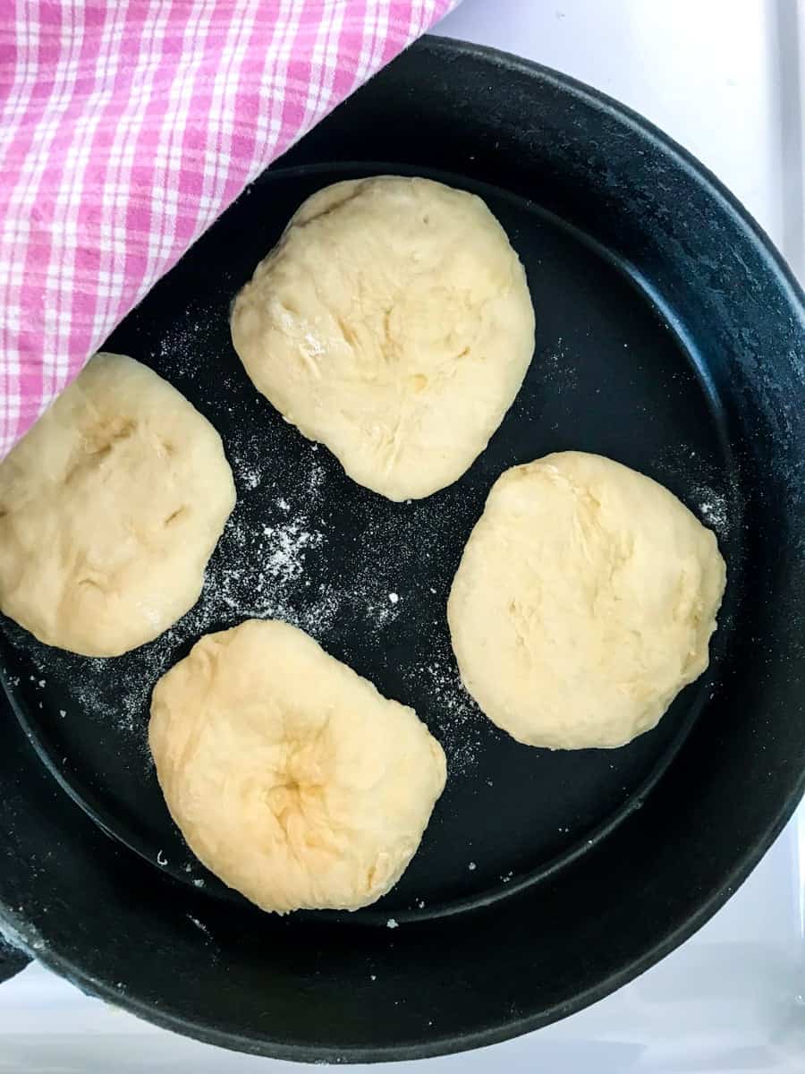 Overnight english muffins in a black pan with a pink and white checkered cloth