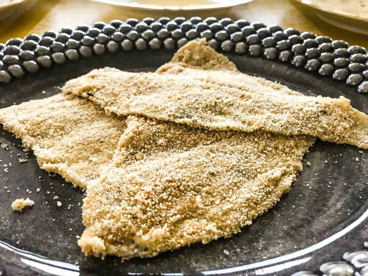 Three breaded plaice filets on a black plate for pan-seared breaded plaice with whipped lemon butter