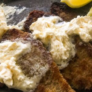 Pan-seared breaded plaice with whipped lemon butter and lemon wedges on a black plate