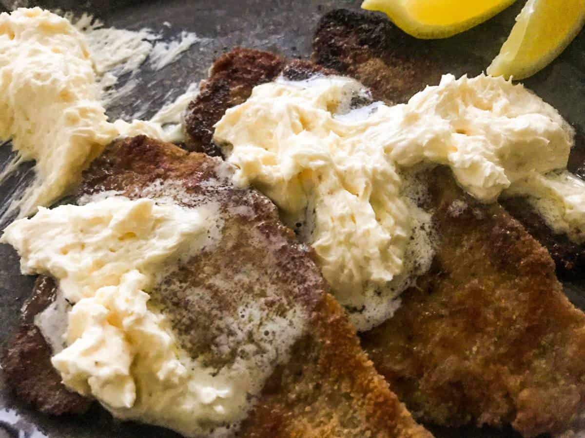 Pan-seared breaded plaice with whipped lemon butter and lemon wedges on a black plate