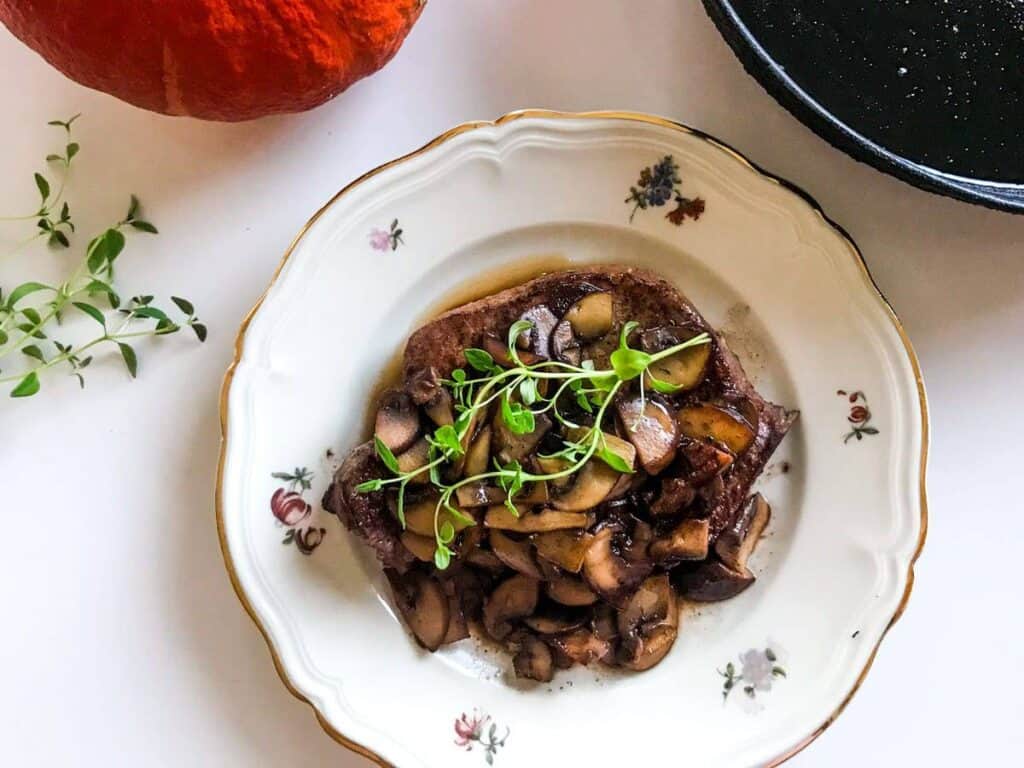 Quick one-pan pork chops and mushrooms with red wine and thyme on a plate on a white surface with a pumpkin and a black cast iron skillet and some thyme