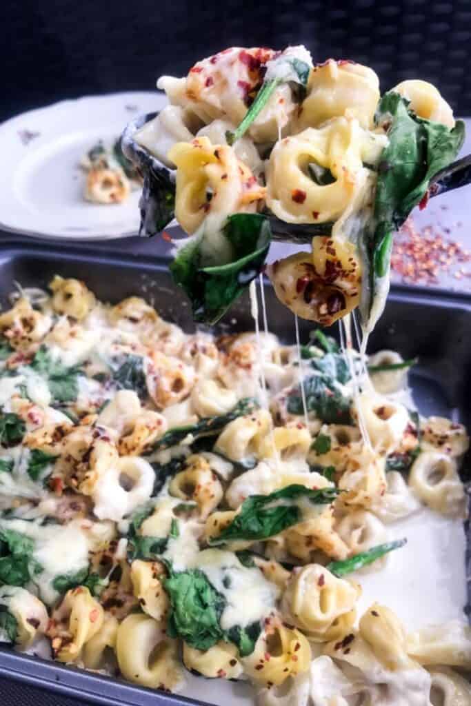 a spoonful of tortellini casserole being lifted out of a pan full