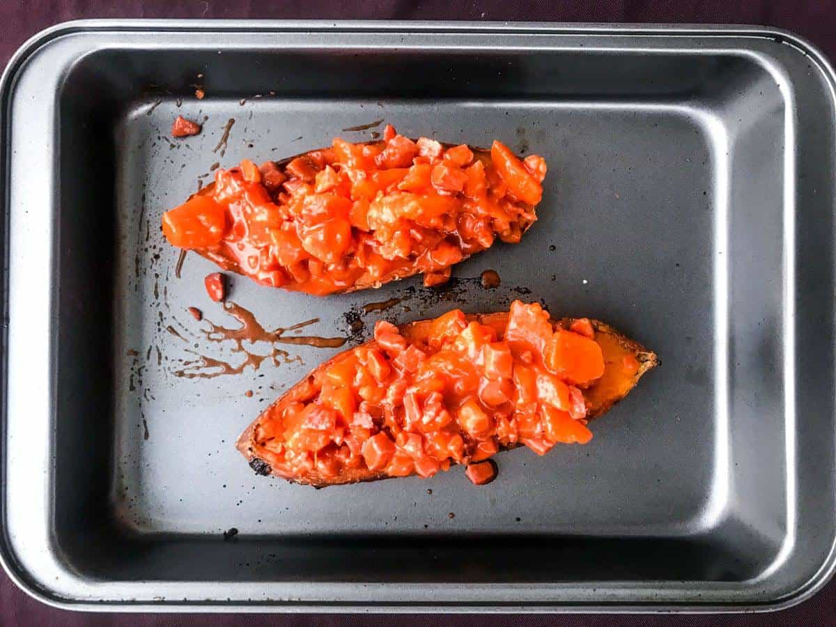 top down view of two sweet potato halves in a deep oven dish loaded with buffalo bacon