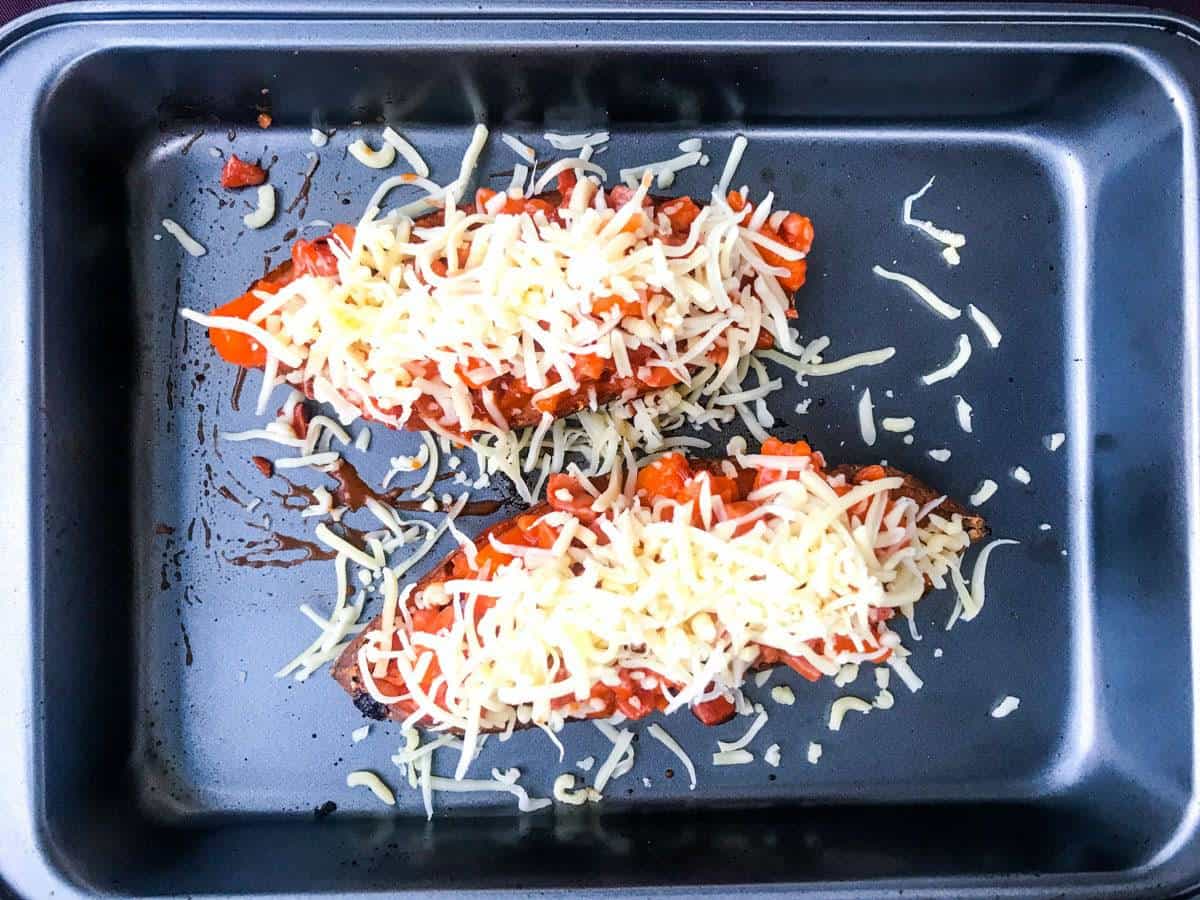 top down view of two sweet potato halves in a deep oven dish loaded with buffalo bacon and cheese, before baking