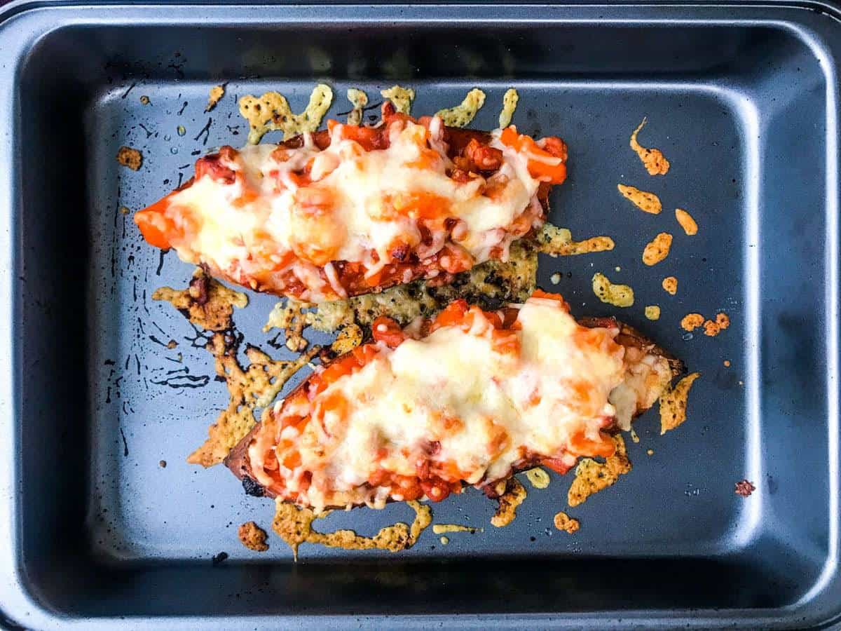 top down view of two sweet potato halves in a deep oven dish loaded with buffalo bacon and cheese, after baking