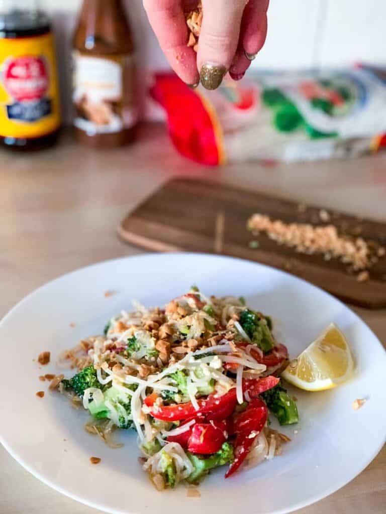 a plate of veggie pad thai with peanuts being sprinkled over