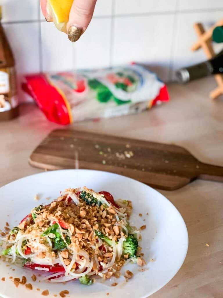 lemon being squeezed over a vegetarian pad thai topped with crushed peanuts