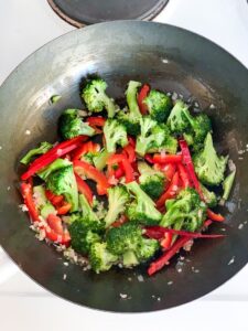 top view of a wok with shallots, garlic, broccoli and red bell pepper