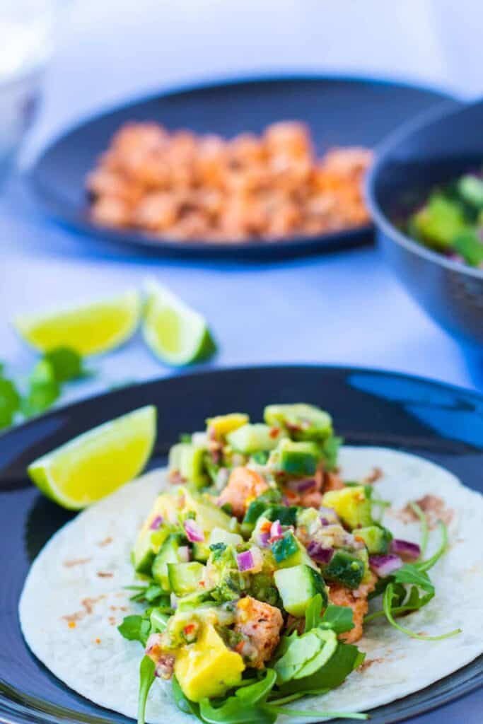 front view of a healthy salmon fish taco with ginger avocado salsa, and a lime wedge