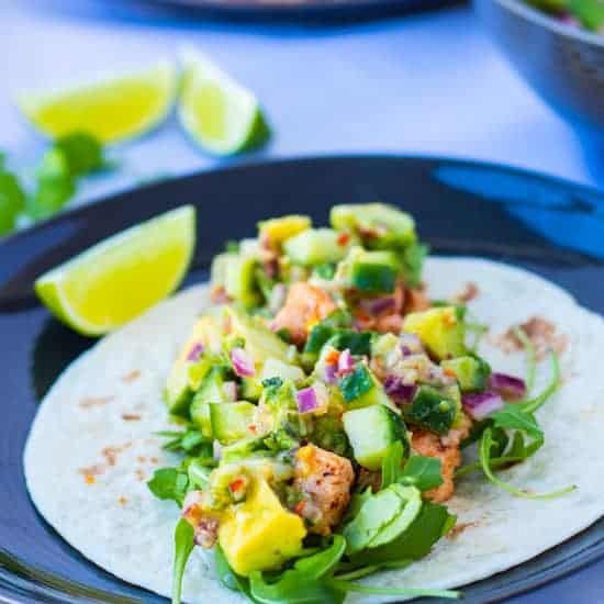 side view of a healthy salmon fish taco with ginger avocado salsa, and a lime wedge