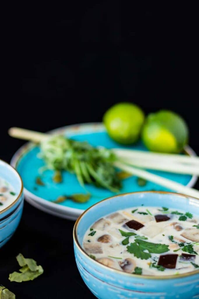 thai ginger coconut soup in a blue bowl with lemongrass and lime in the background