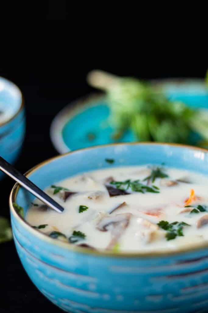 close up side view of thai ginger coconut soup in a blue bowl