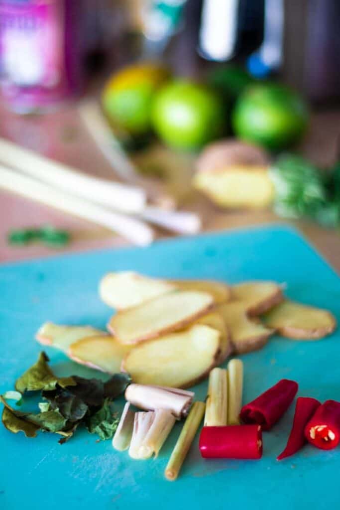 sliced ginger, lime leaves, lemon grass and chili on a blue chopping board