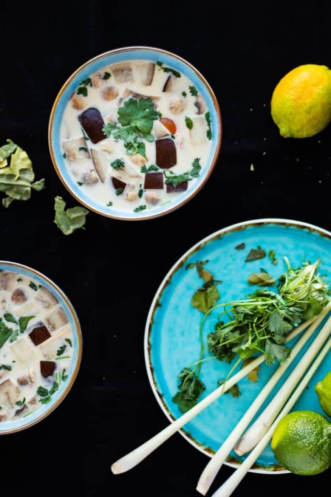 top view of thai ginger coconut soup in two blue bowls on a black surface