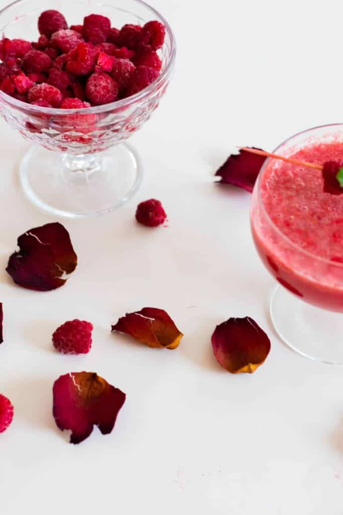 a glass of raspberry grapefruit mocktail on a table decorated with rose petals