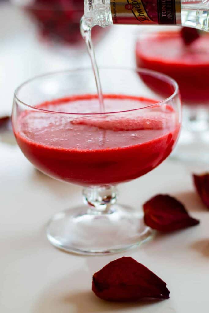 a glass of sparkling raspberry grapefruit mocktail  with tonic being poured into it