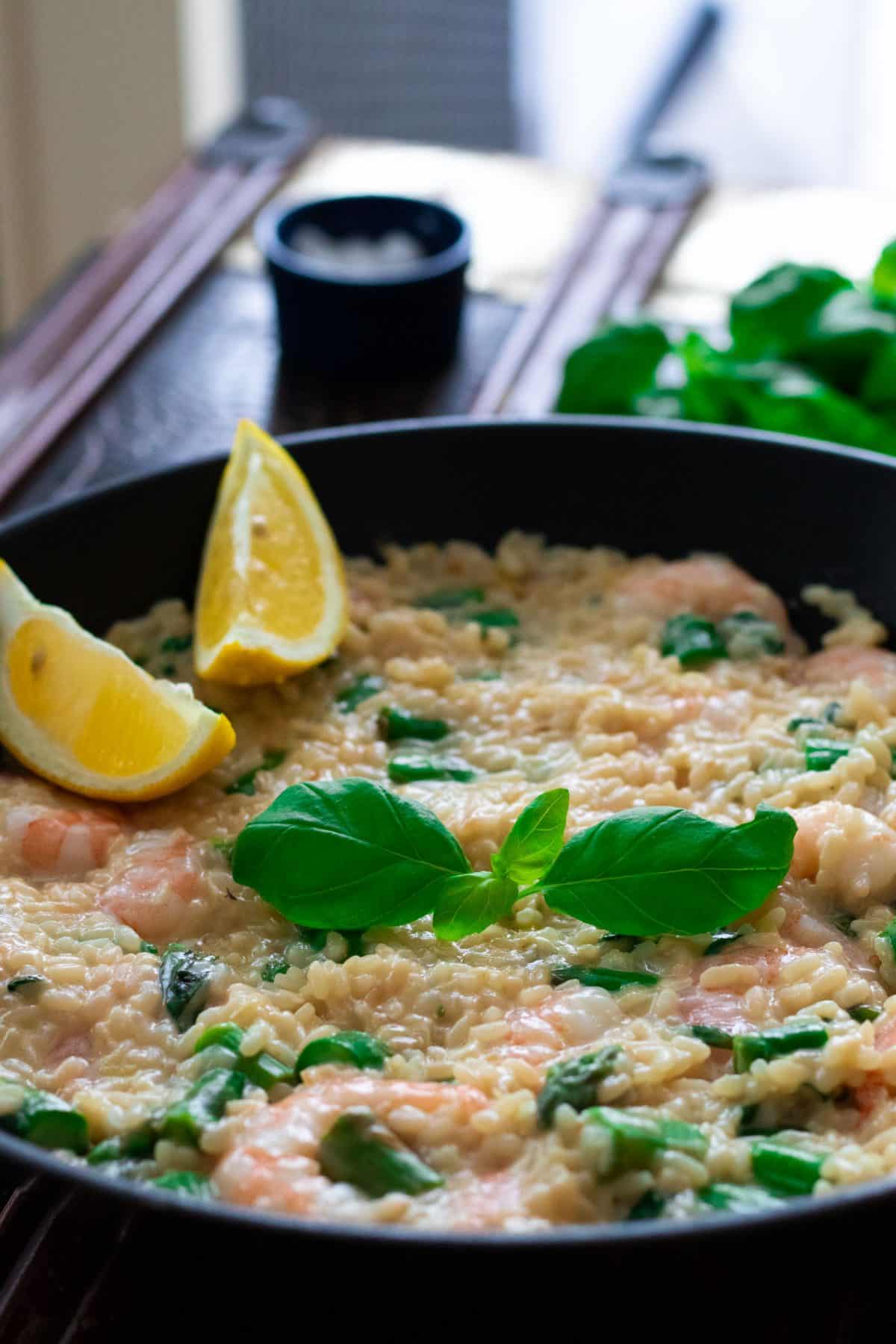 a pan with shrimp risotto, topped with basil leaves and lemon wedges.