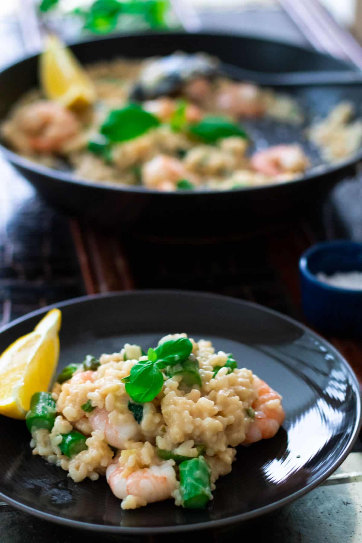 a plate with shrimp risotto in front of a a pan of shrimp risotto.