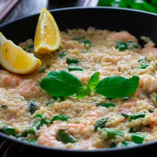 a pan with shrimp risotto, topped with basil leaves and lemon wedges