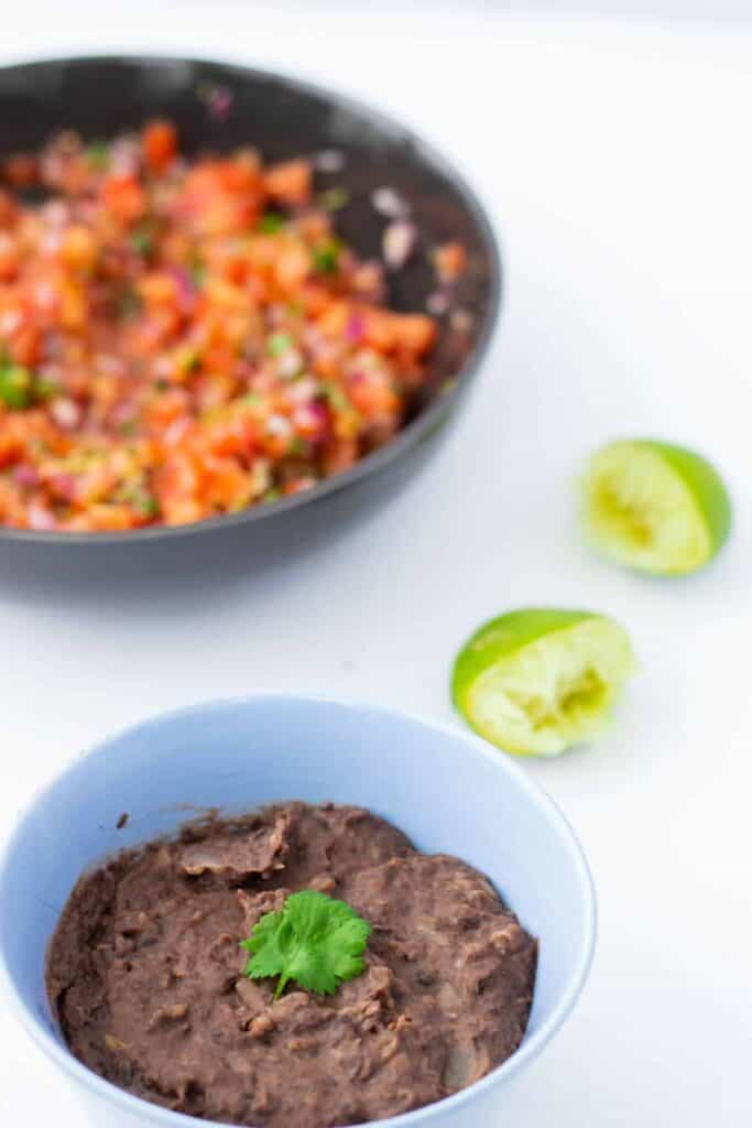 refried beans in a bowl in front of pico de gallo in a bowl