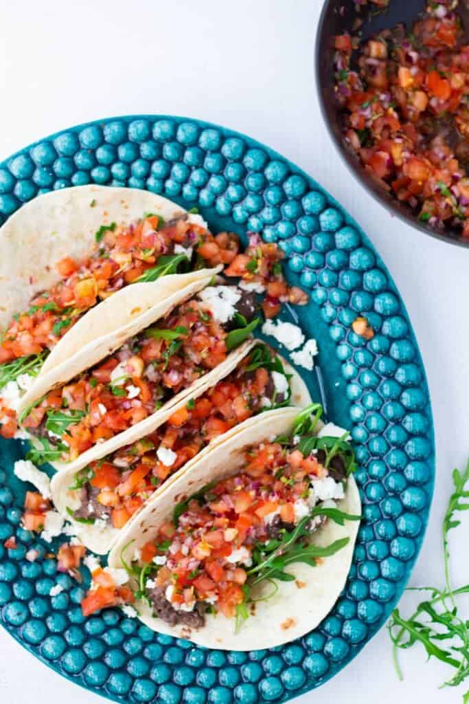 top view of close-up of four vegetarian tacos with black beans, feta cheese and pico de gallo