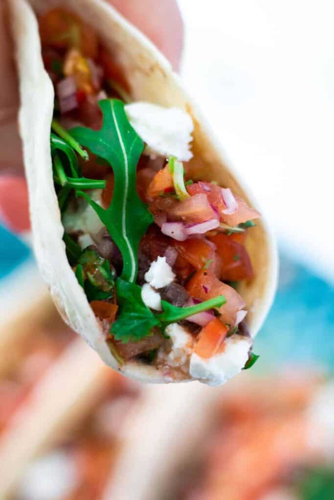 close-up of a hand held vegetarian taco with black beans, feta cheese and pico de gallo
