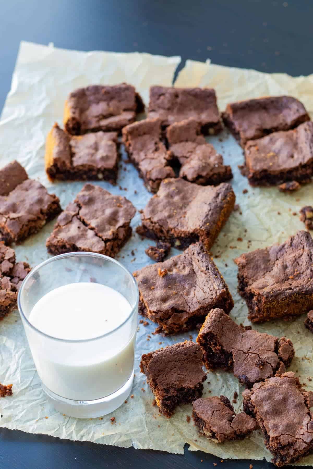 brownies with cocoa powder on parchment paper with a glass of milk