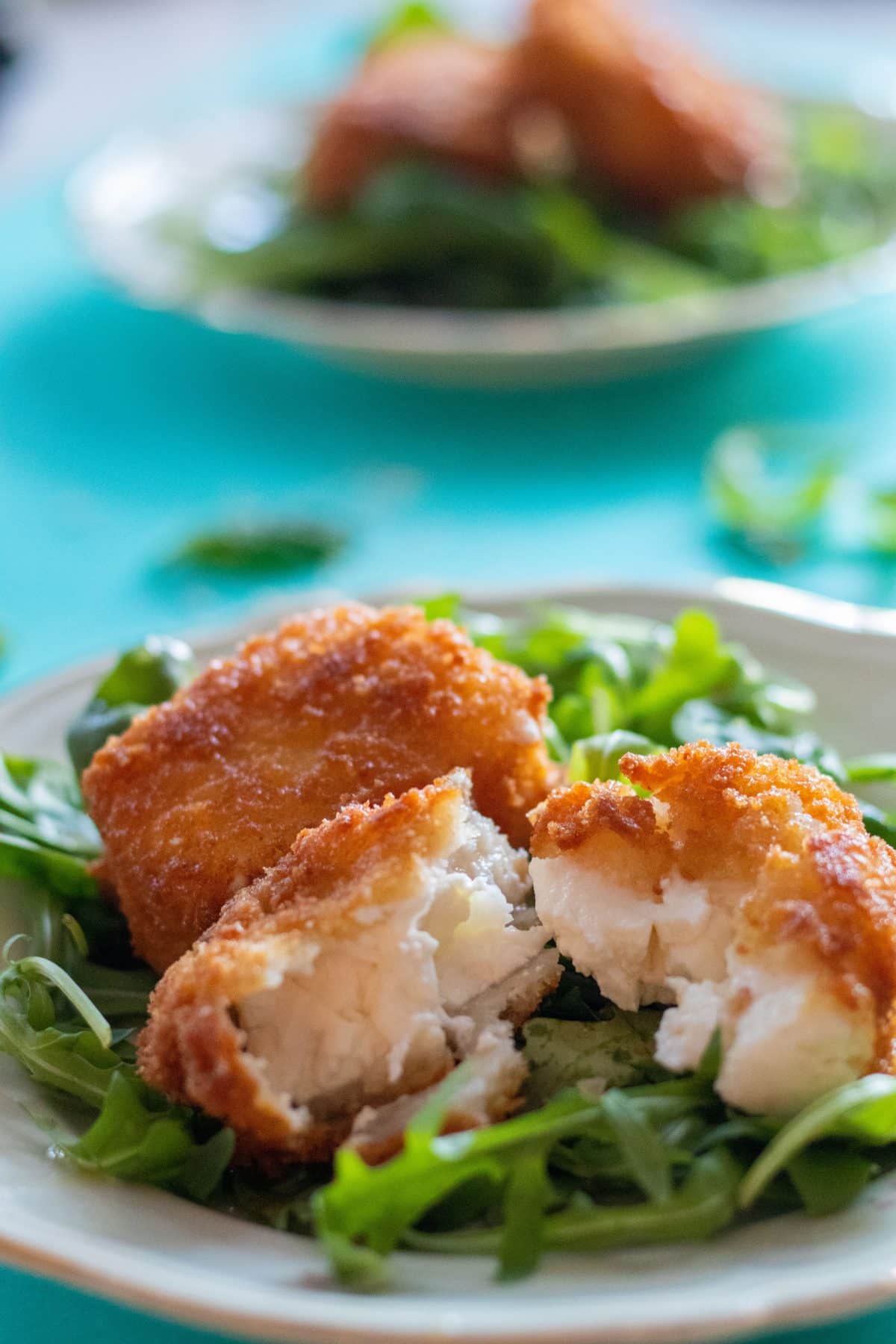 panko breaded feta cheese on a bed of greens with one breaded cheese split open