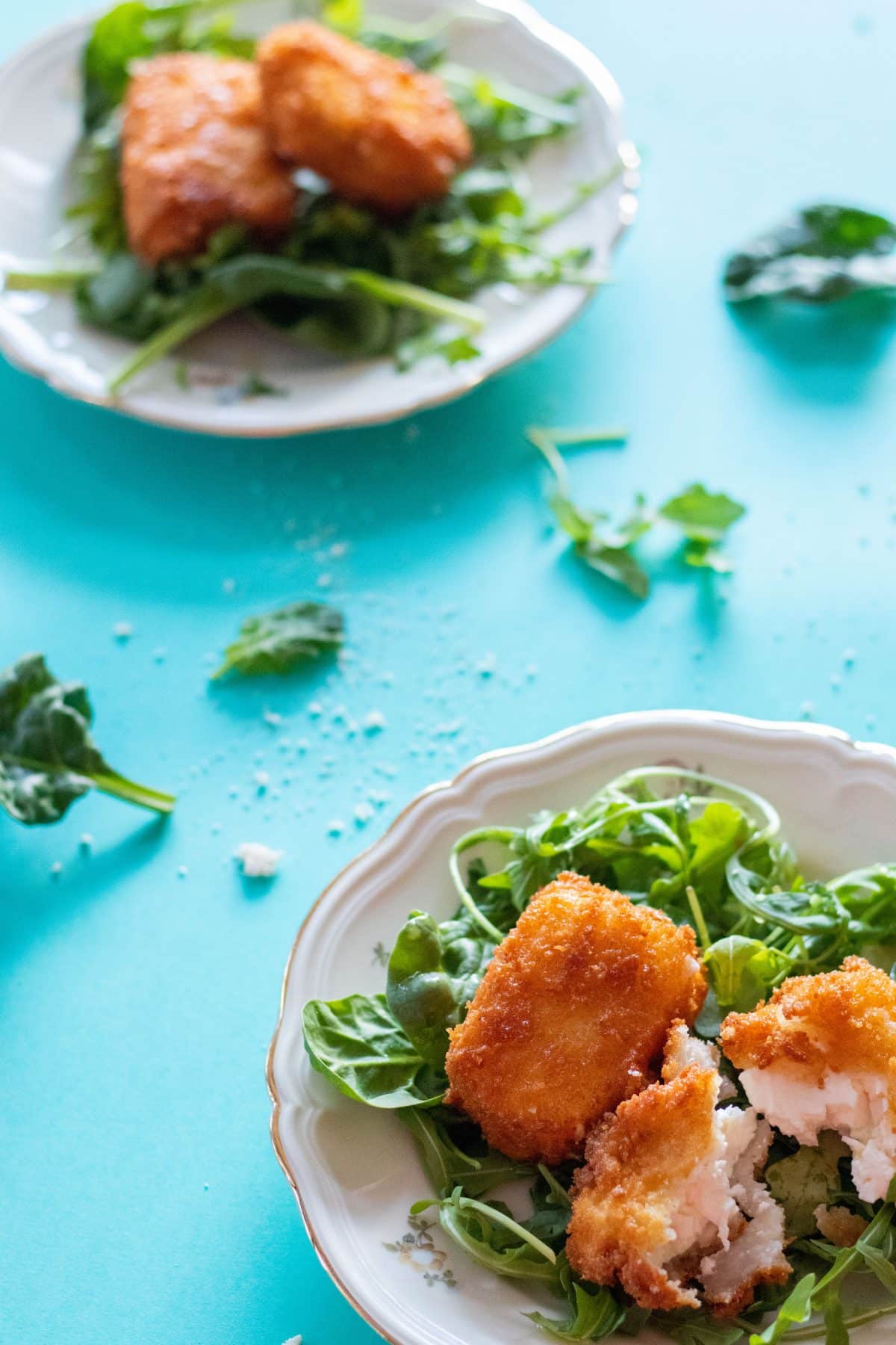 top view of panko breaded feta cheese on a bed of greens on a plate on a turquoise background