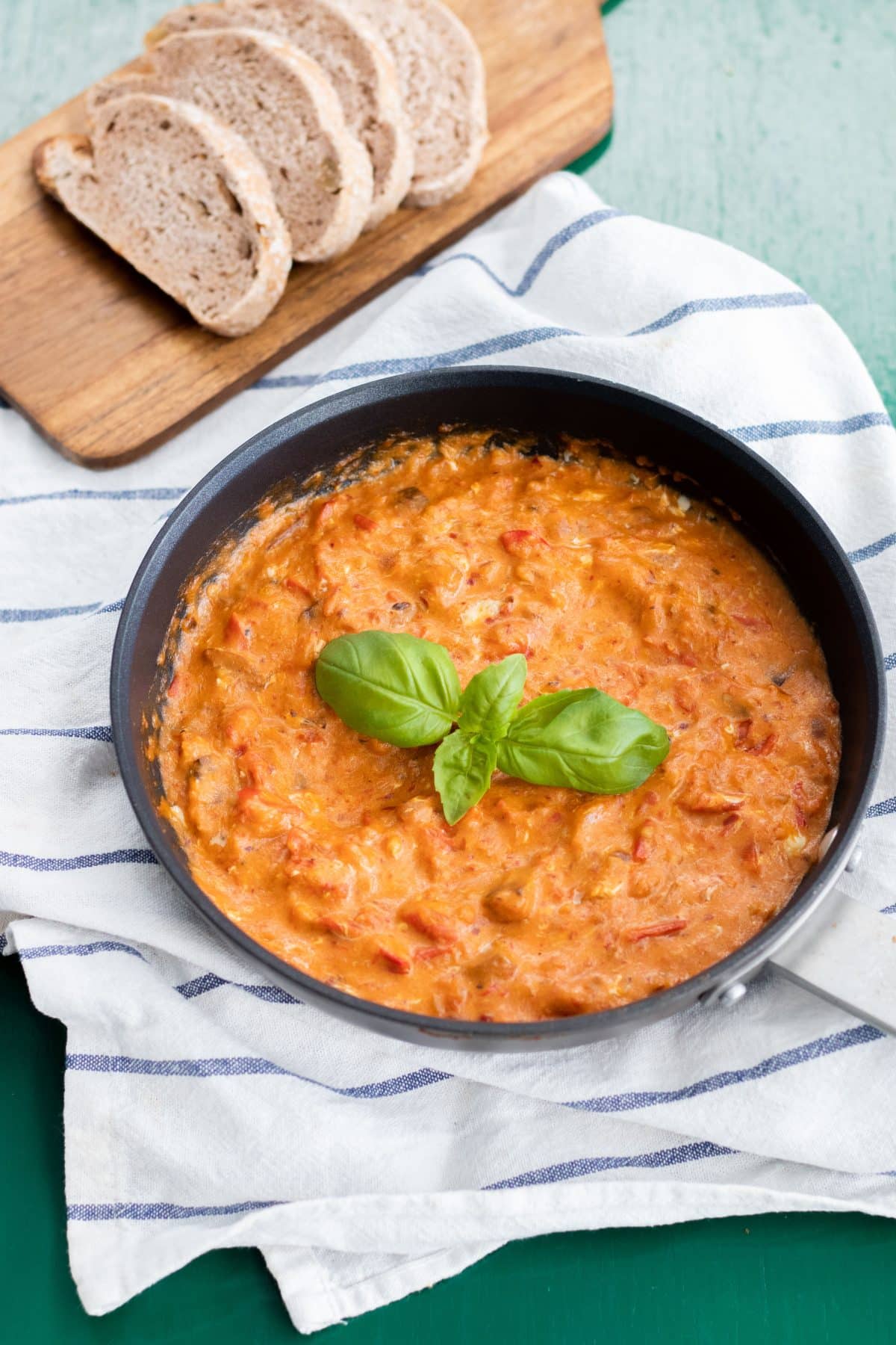 Shakshuka garnished with basil in a frying pan on a white and blue striped kitchen towel