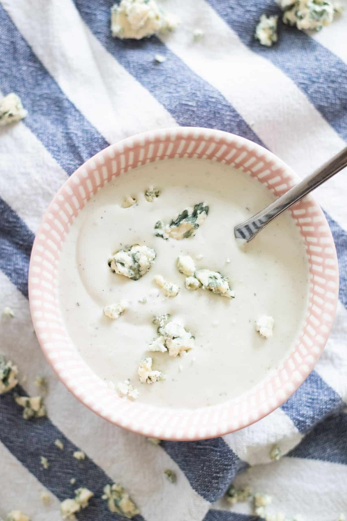 top view of a pink bowl with blue cheese sauce and blue cheese crumbles