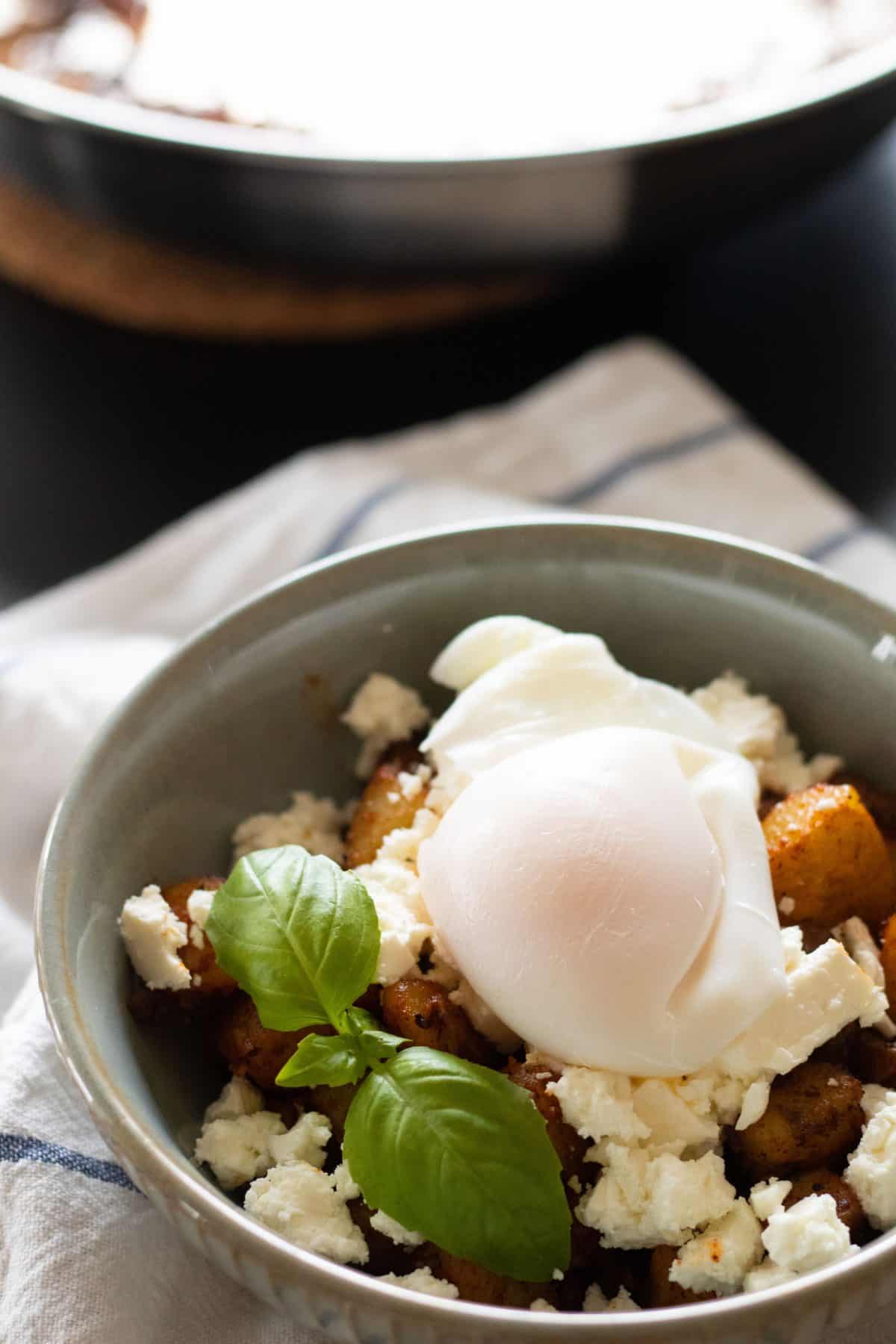 side view of a bowl with fried potatoes, feta cheese and a poached egg