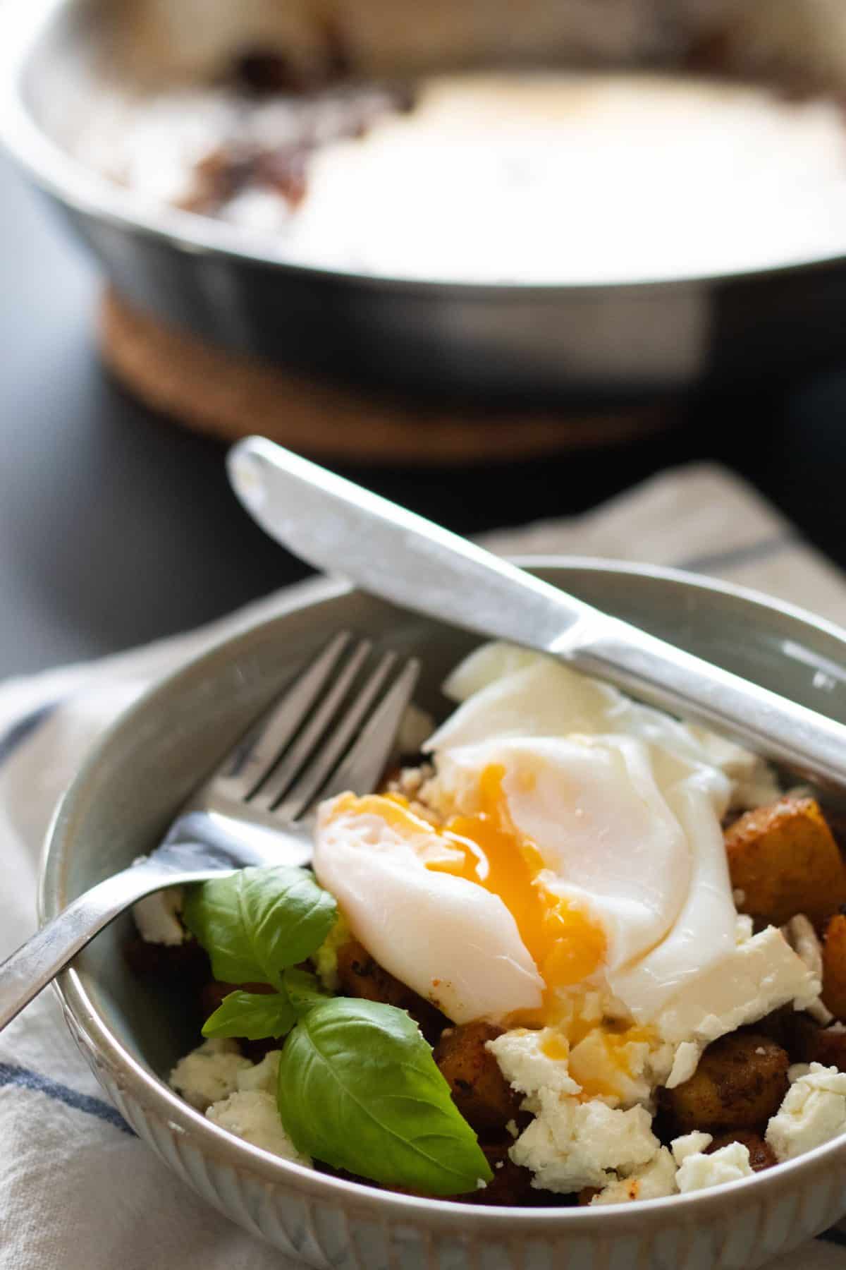 closeup sideview of a bowl with fried potatoes, feta cheese and poached egg