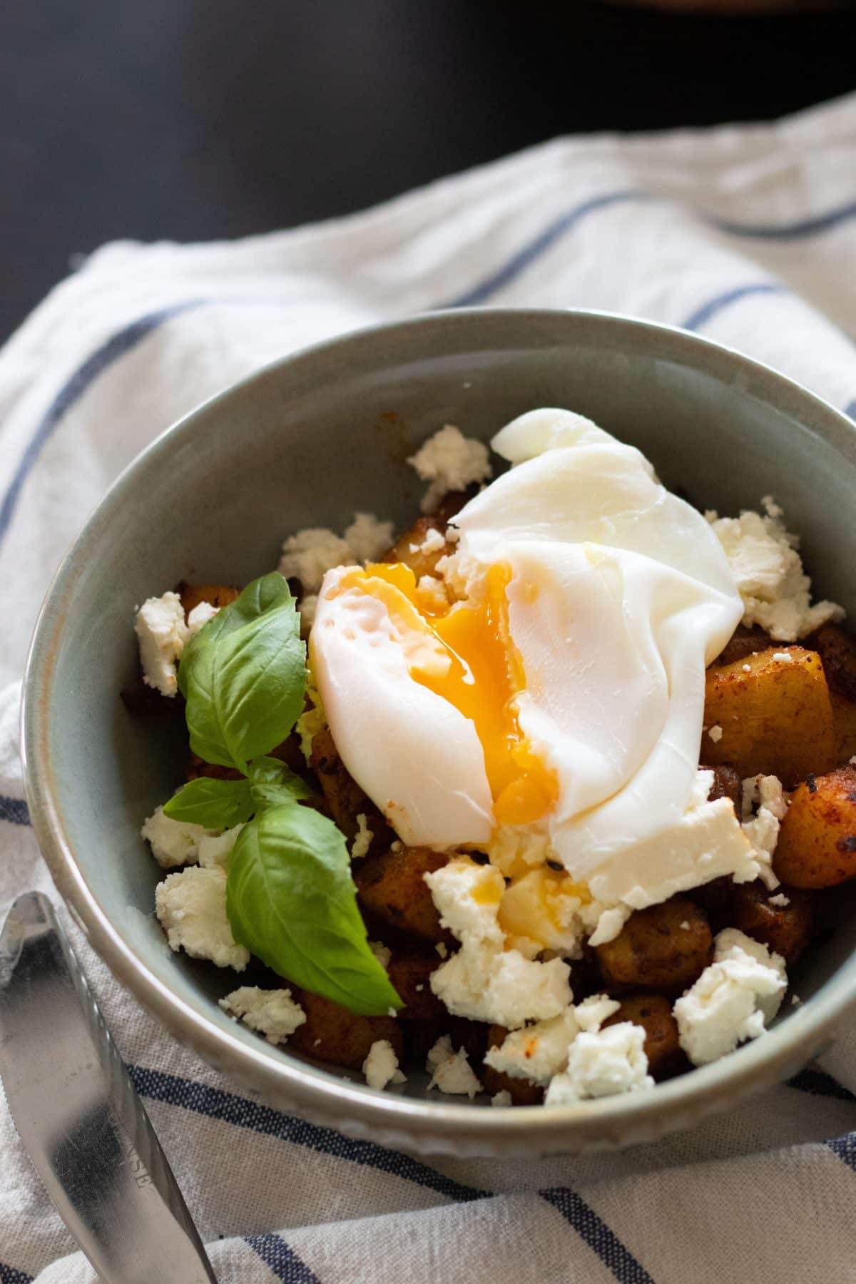 top view of a bowl of fried potatoes with feta cheese and a poached egg with the yolk running out