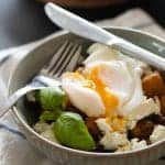 closeup sideview of a bowl with fried potatoes, feta cheese, poached egg and a sprig of basil