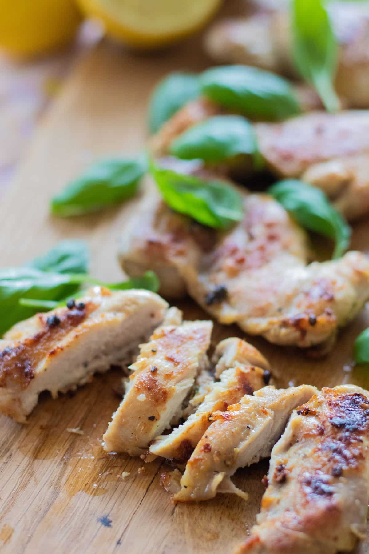 sideview of sliced grilled chicken marinated with lemon and decorated with basil leaves.