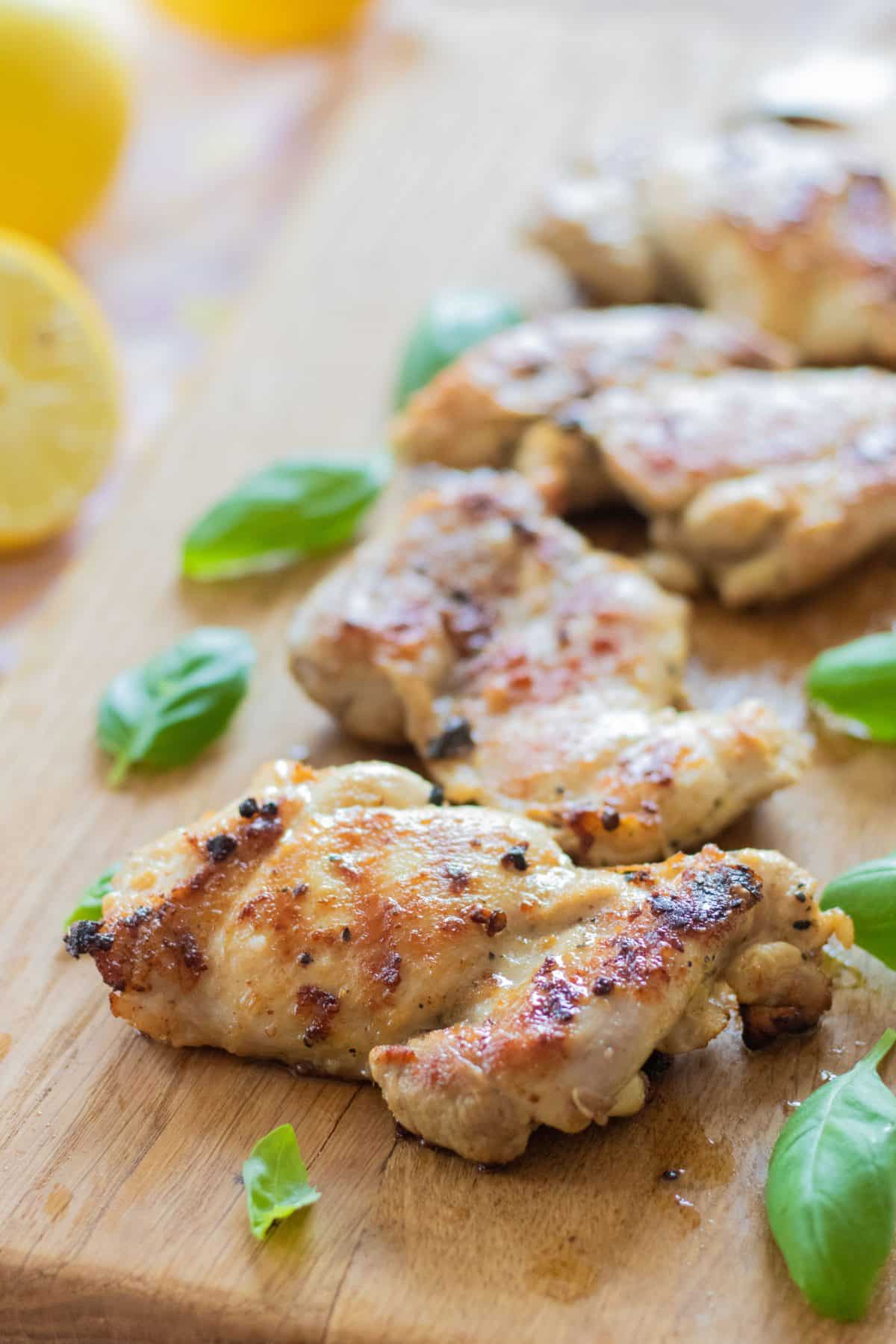 sideview of lemon chicken on a wooden chopping bord with basil leaves.